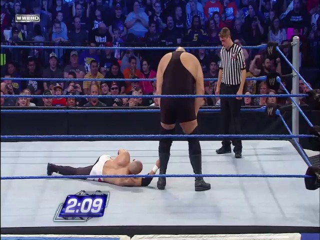 A frame from WWE SmackDown (October 15, 2010) at 56:21. A wrestler lies on the mat while an opponent stands over him in the WWE ring, with a referee watching nearby. The crowd fills the arena in the background, and a timer displaying "2:09" is visible at the bottom of the frame.