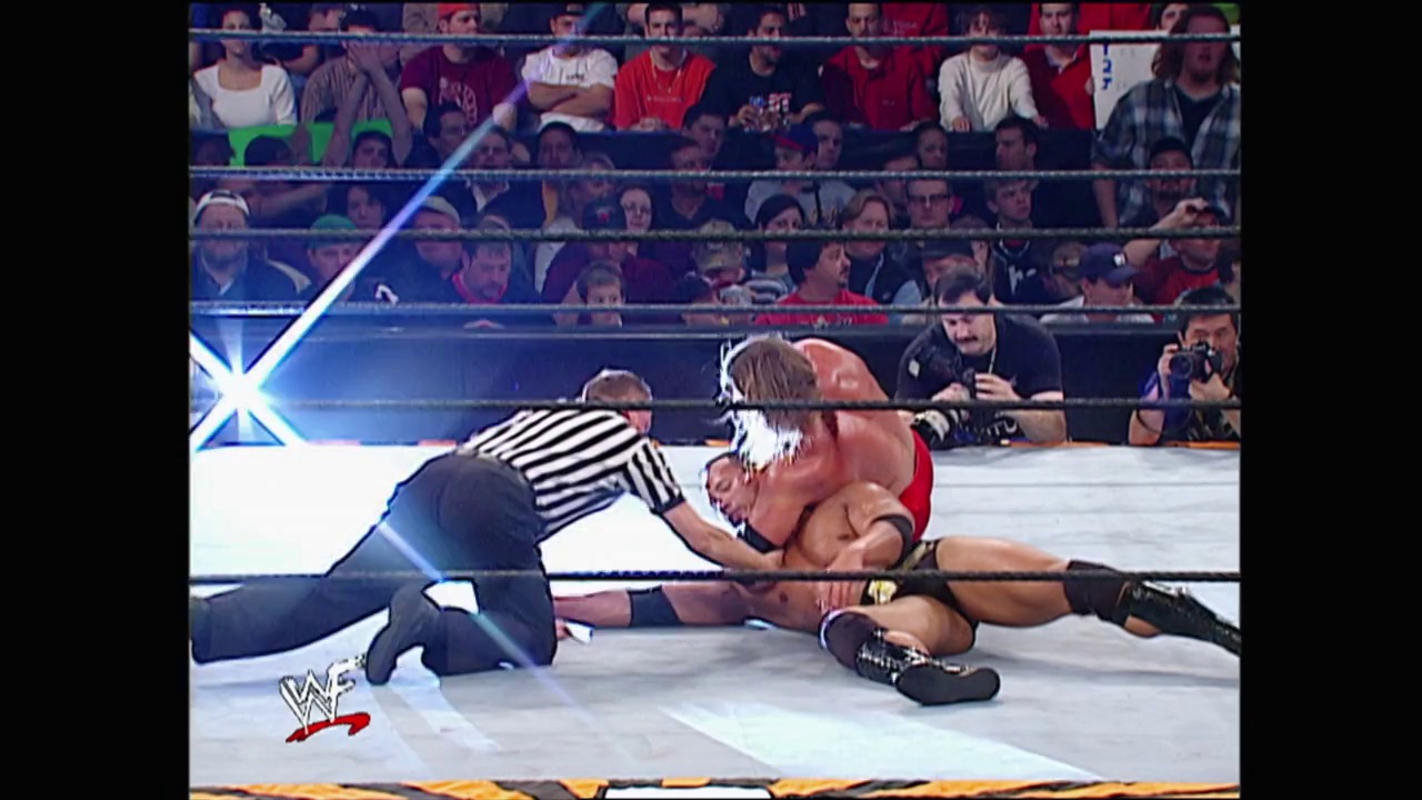 A frame from Royal Rumble (2002) at 1:10:16. A referee in striped shirt checks on a wrestler lying on the mat during a WWE Royal Rumble 2002 match, while the crowd watches from the stands and the WWF logo appears in the lower left corner.