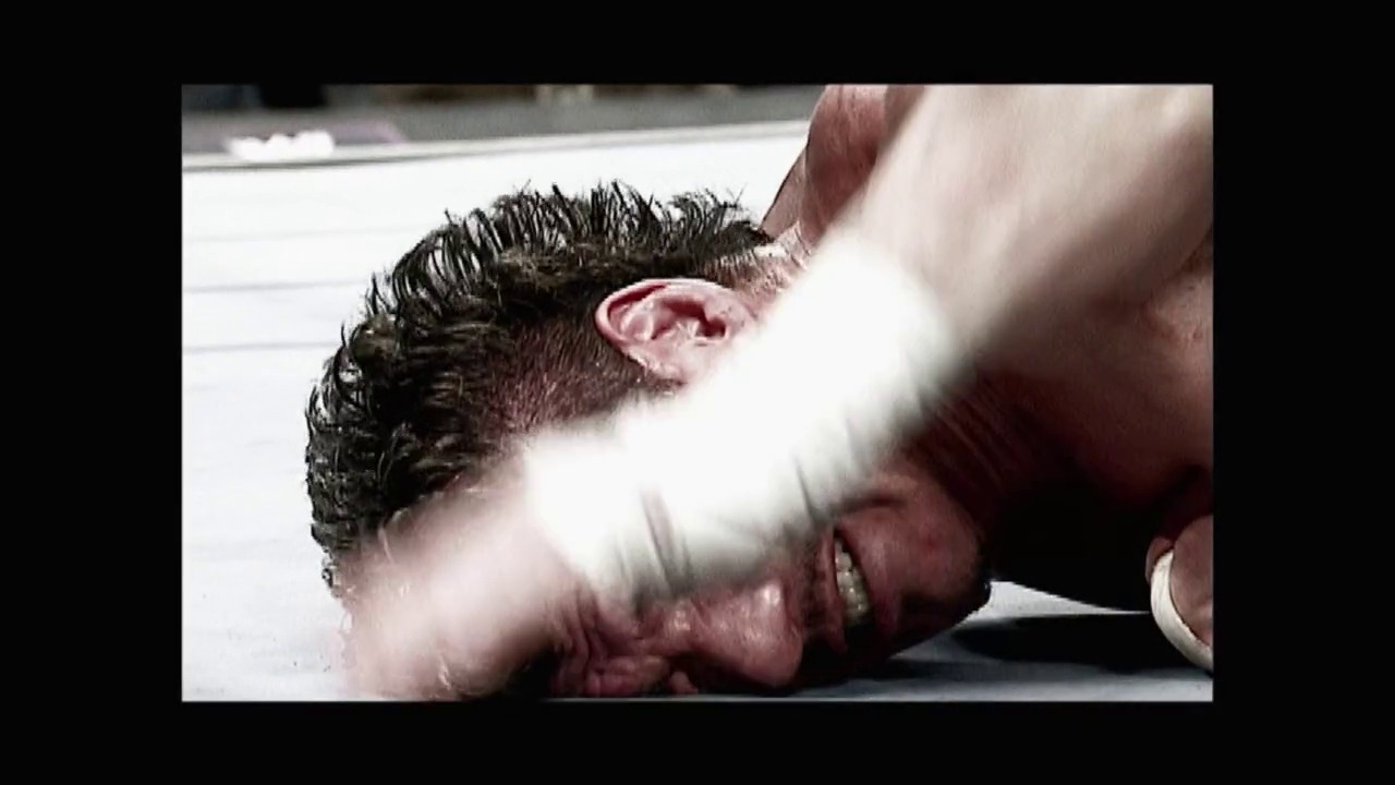 A frame from Royal Rumble (2004) at 0:41. A wrestler in dark hair is pinned to the white wrestling mat while an opponent applies pressure, with a blurred hand visible in the foreground during an intense grappling sequence at the Royal Rumble event.