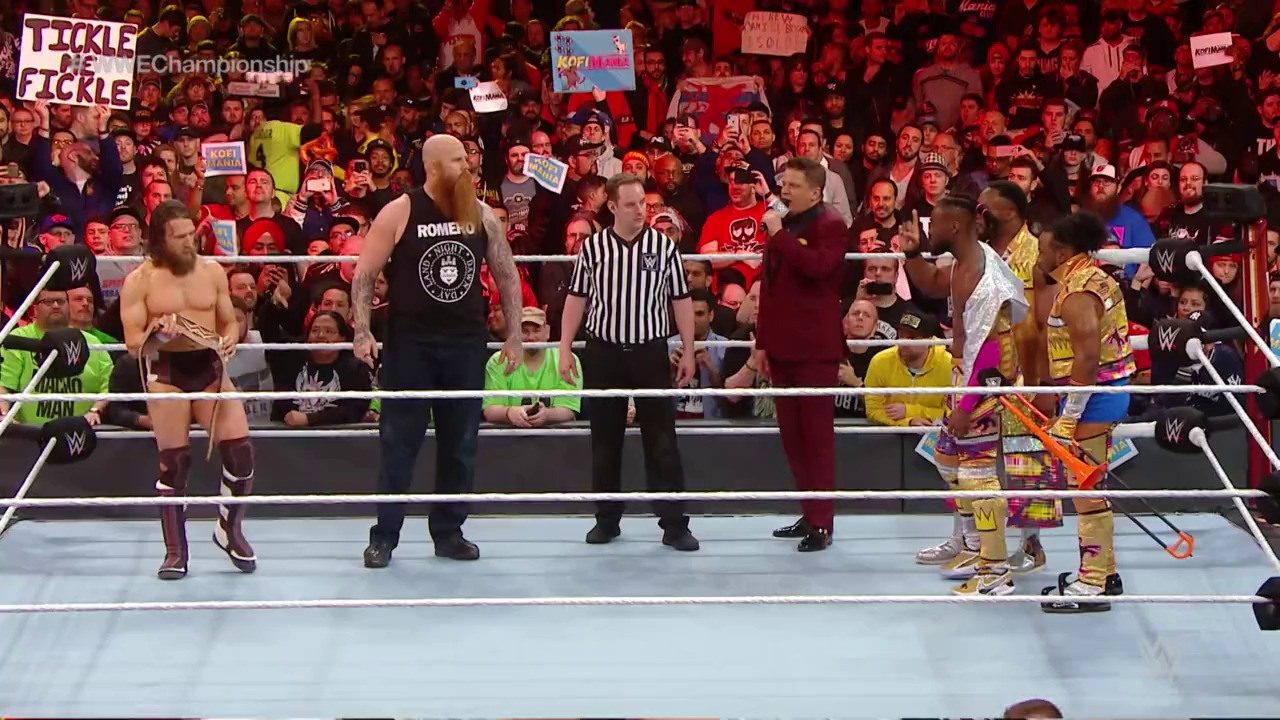 A frame from WrestleMania 35 (2019) at 2:16:33. # WrestleMania 35 Ring Scene

A WWE wrestling match is underway in a packed arena, with multiple wrestlers on the blue canvas facing each other while a referee in stripes oversees the action. The enthusiastic crowd fills the red-lit stadium behind the ropes, many holding signs and cheering.