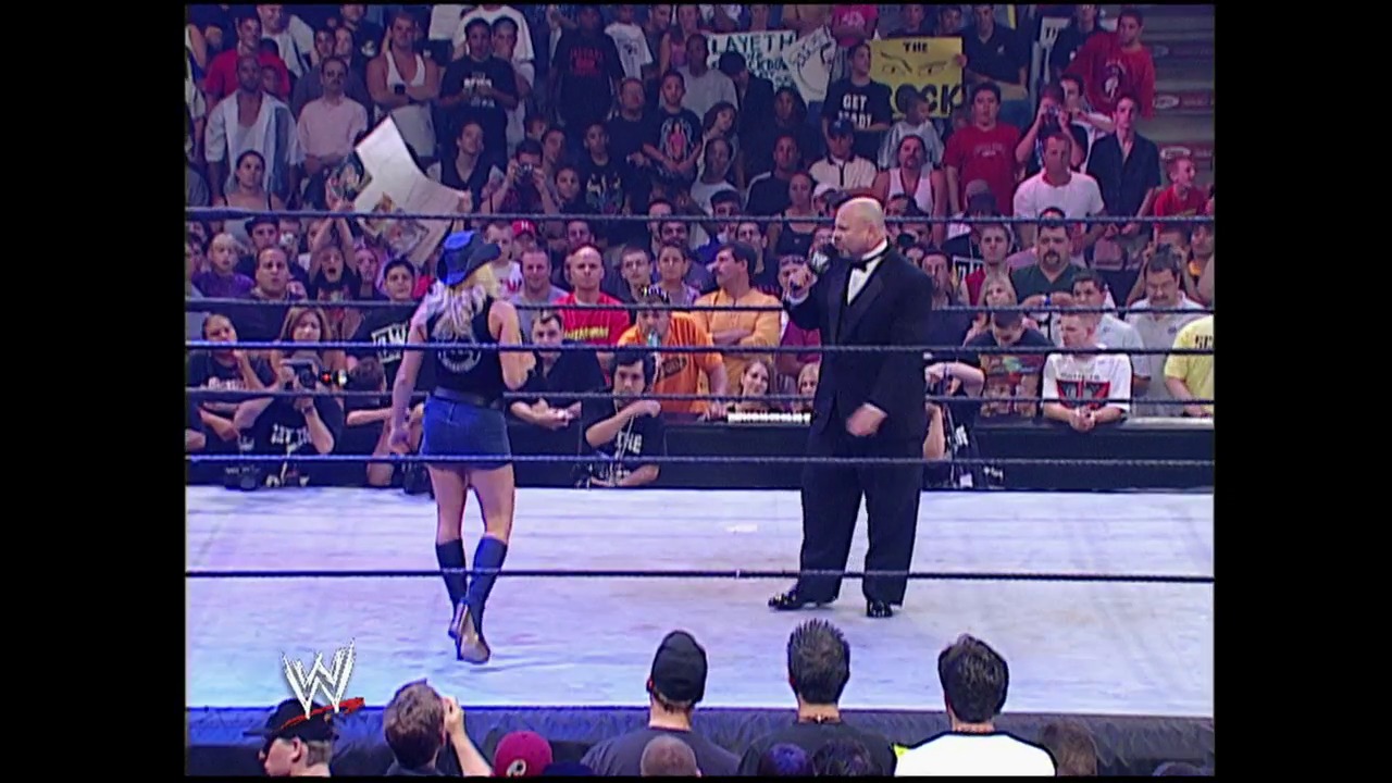 A frame from Summerslam (2002) at 2:17:53. A WWE wrestling match is underway in the ring with a female wrestler in blue attire facing off against a bald man in a black tuxedo. The arena is packed with enthusiastic fans visible in the background, and the WWE logo appears in the lower left corner of the broadcast.