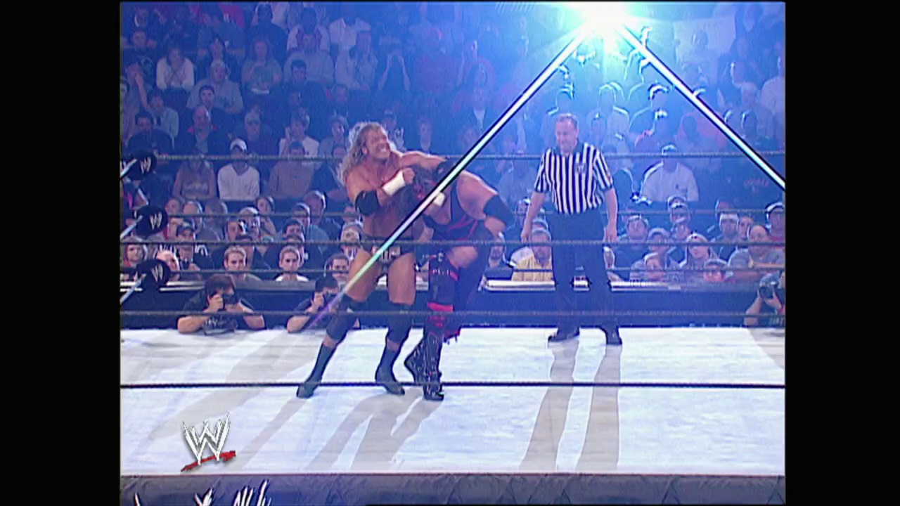A frame from WWE No Mercy (2002) at 1:11:31. A WWE wrestler grapples with an opponent in the ring while a referee in black and white stripes officiates. The crowd fills the arena seats behind the illuminated ring structure with the WWE logo visible in the corner.