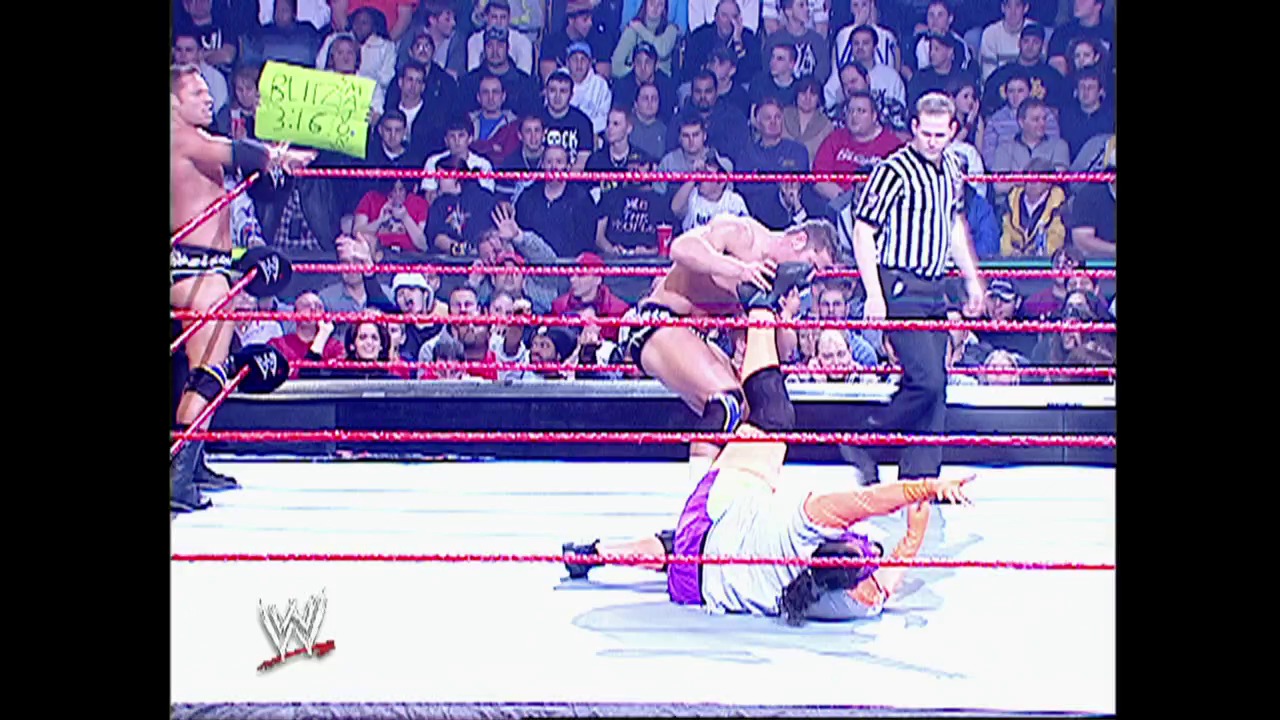 A frame from WWE Raw (November 10, 2003) at 27:15. A WWE wrestler lies on the mat in the foreground while another stands in the ring during a Raw match. The referee in a striped shirt oversees the action as a full crowd watches from the stands, with the WWE logo visible in the corner.