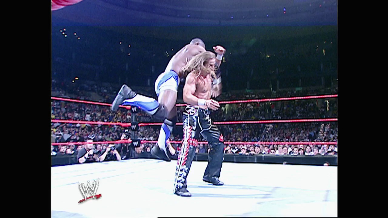 A frame from WWE Raw (May 2, 2005) at 40:00. A WWE wrestler in blue and white attire executes a flying move against an opponent in pink and black during a Raw match, with the packed arena crowd visible in the background and the WWE logo displayed in the lower left corner.