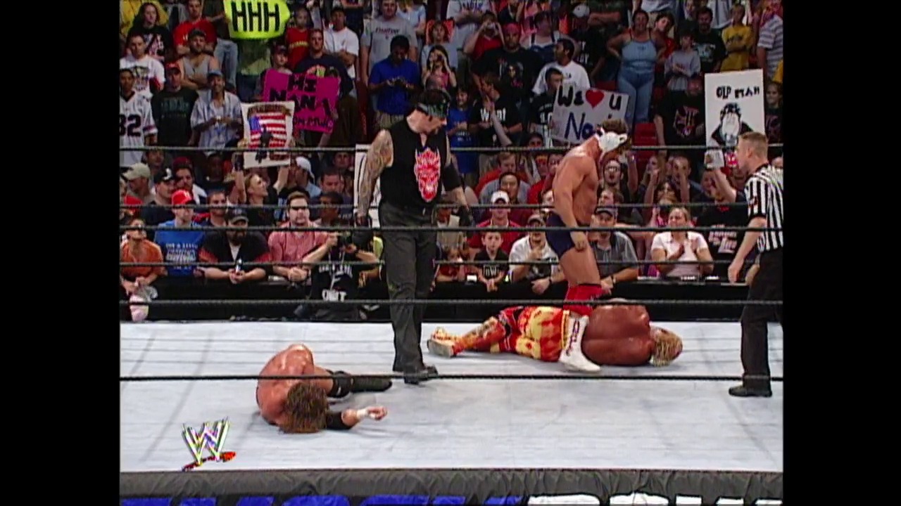 A frame from WWE Raw (June 6, 2002) at 1:27:10. # WWE Raw Wrestling Match

Two wrestlers lie on the mat during an intense match, with one opponent standing nearby and a referee positioned ringside. The packed crowd in the background holds signs while the WWE logo appears in the lower left corner.