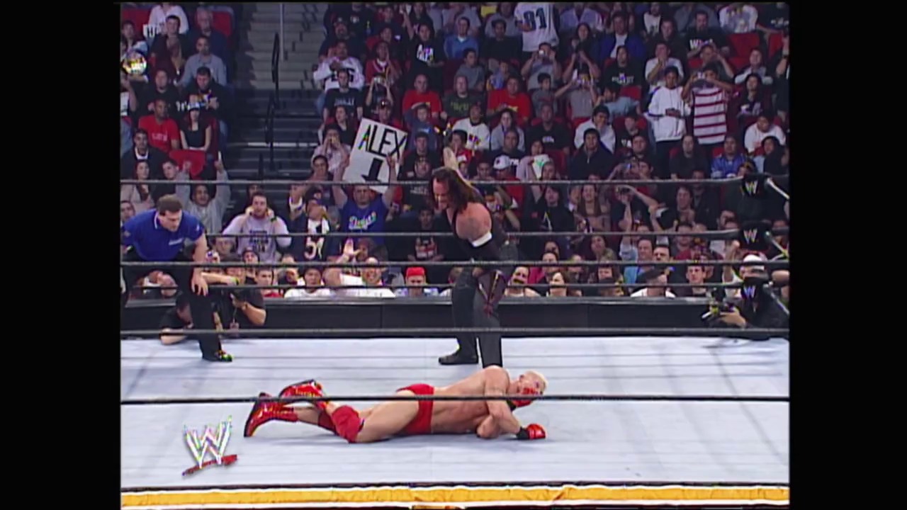 A frame from WWE Royal Rumble (2005) at 49:24. A wrestler in red lies on the mat while a referee counts, with another competitor in blue visible nearby. The crowd fills the arena stands as the WWE logo appears in the corner of the broadcast.
