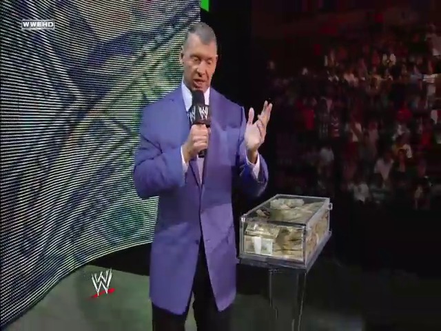 A frame from WWE Raw (June 2, 2008) at 25:31. A man in a purple blazer holds a microphone while gesturing toward a briefcase filled with cash on stage. The WWE logo and crowd are visible in the background of this wrestling event.