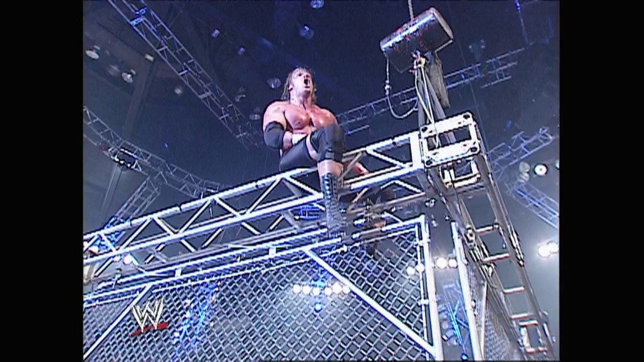 A frame from WWE Raw (September 8, 2003) at 1:33:37. A muscular wrestler stands atop a steel cage structure during a WWE match, looking upward with an intense expression. The WWE logo is visible on the cage, with arena lighting and rigging visible in the background.
