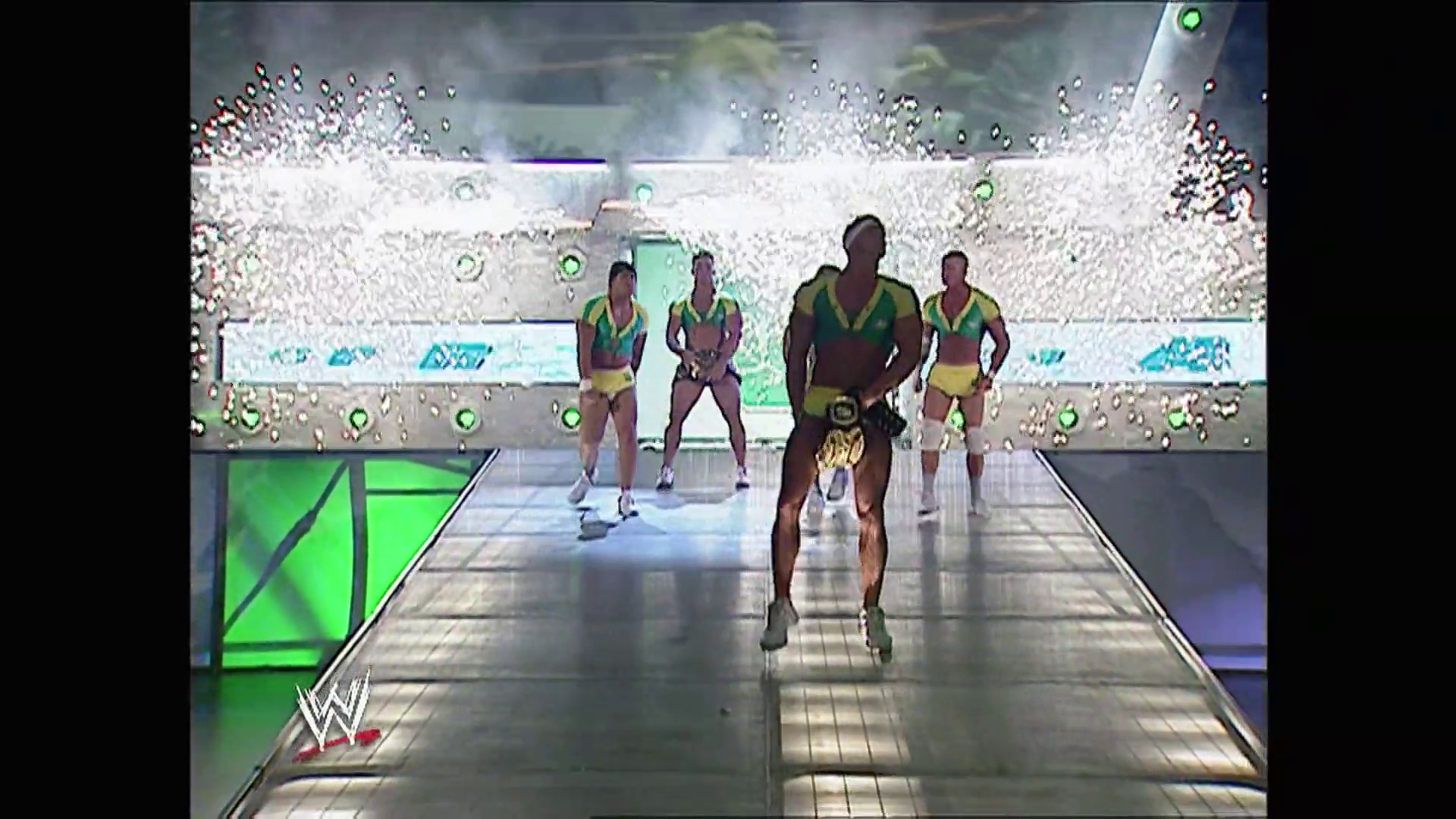 A frame from WWE Raw (October 2, 2006) at 51:01. A wrestler in yellow and green attire enters a WWE ring down the entrance ramp, with teammates in matching gear walking behind him. The stadium is packed with cheering fans visible in the crowded stands above the illuminated ring.