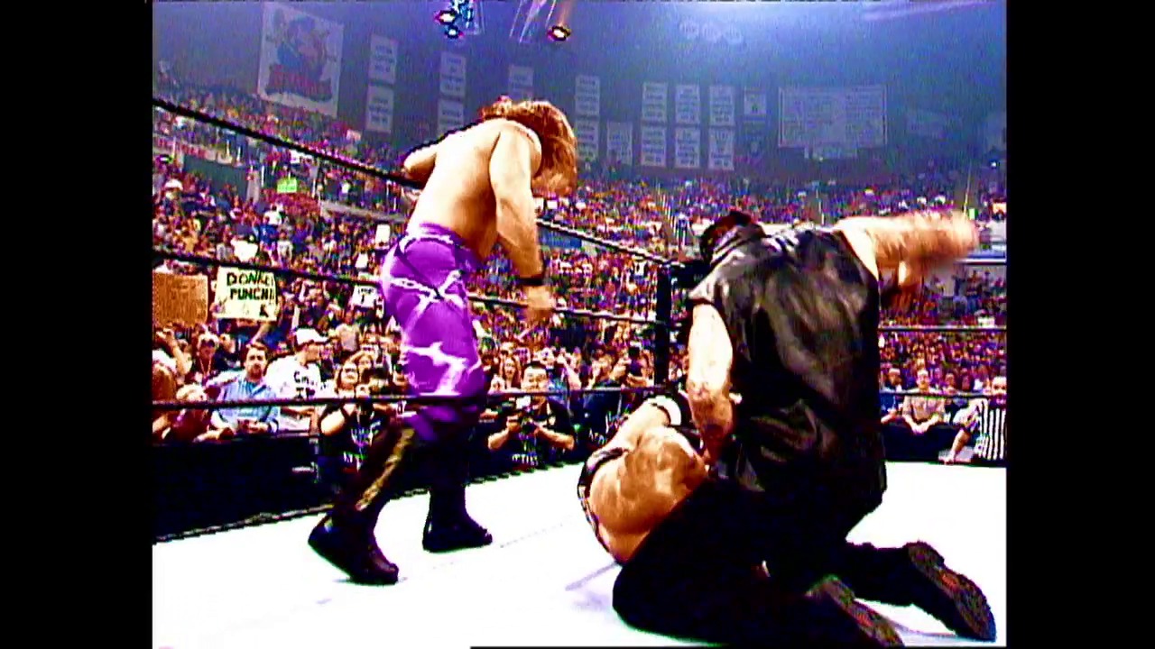 A frame from WWE Raw (May 2, 2002) at 0:38. A wrestler in purple pants stands in the WWE ring while another competitor lies on the mat below. A packed arena crowd fills the background under bright lighting, with the ring ropes and arena signage visible.