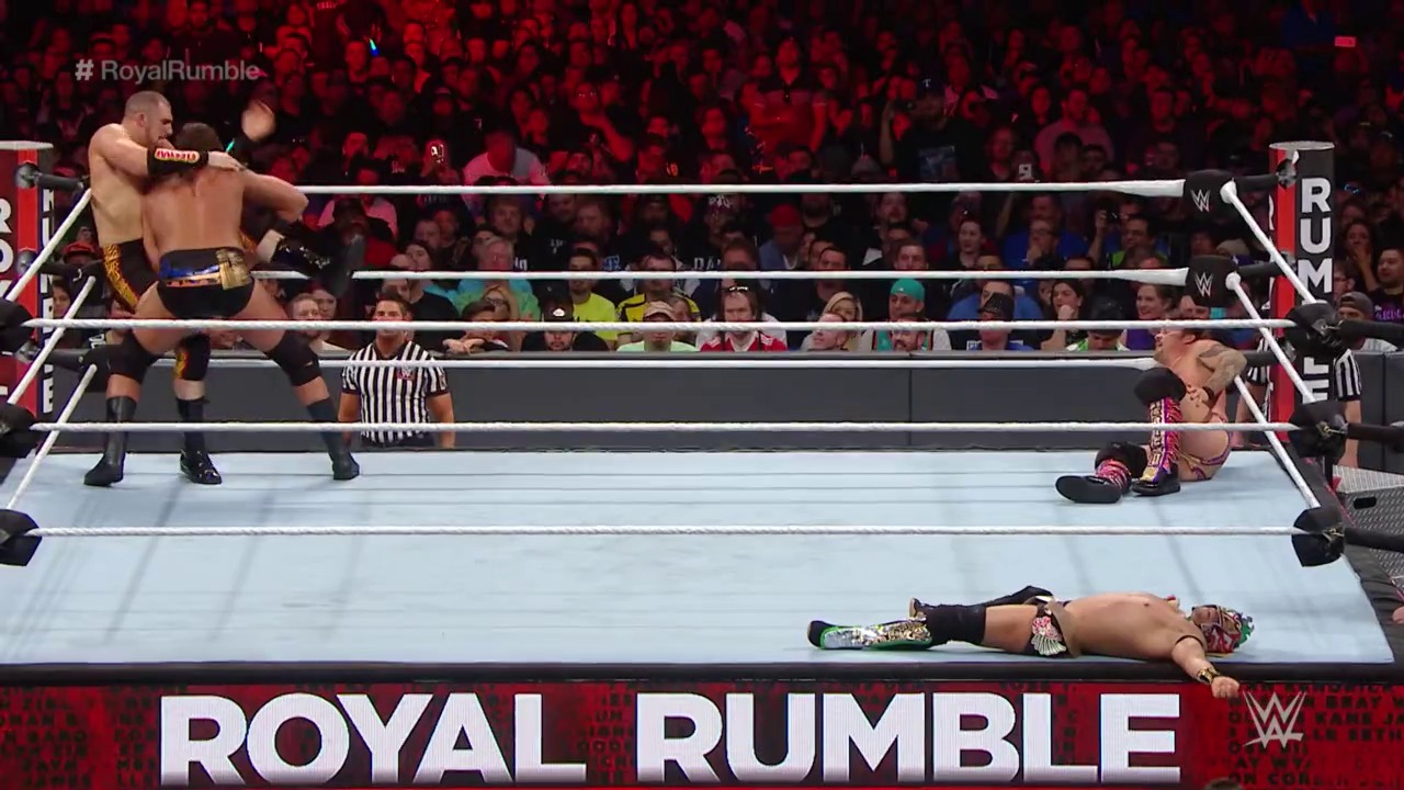 A frame from WWE: Royal Rumble (2017) at 2:30:34. A WWE wrestler lies on the mat after being eliminated, while another competitor stands in the ring preparing for the next opponent. The referee in striped shirt oversees the match as the crowd cheers in the red-lit arena during the Royal Rumble event.