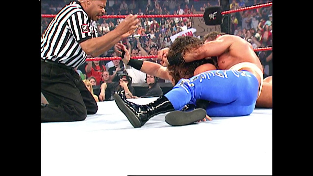 A frame from WWE SmackDown (May 31, 2001) at 1:01. A referee in a black and white striped shirt kneels on the white WWE ring mat, checking on a wrestler in blue pants who is lying down. A crowded arena with red ropes surrounds the ring in the background.