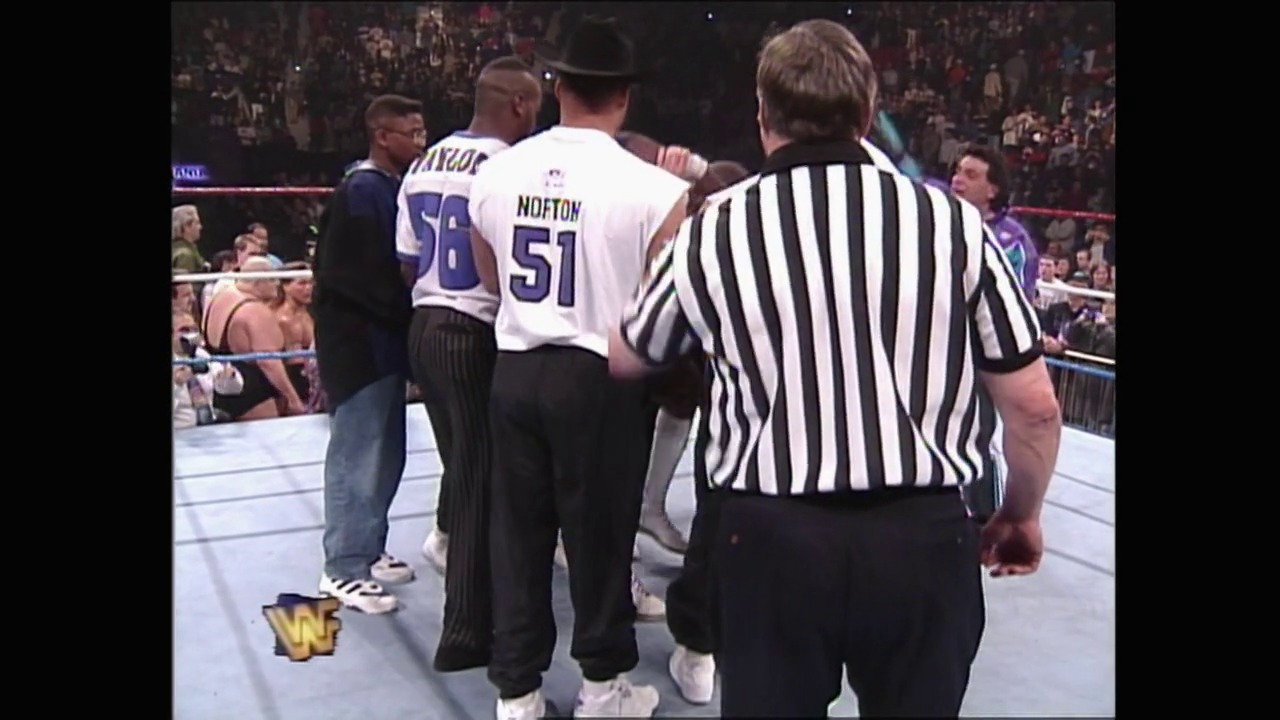 A frame from WrestleMania XI (1995) at 2:24:44. A referee in striped shirt oversees wrestlers in the WrestleMania XI ring, with one competitor wearing a basketball-style jersey numbered 51 (Nofton). The crowd fills the arena in the background as action unfolds in the squared circle.