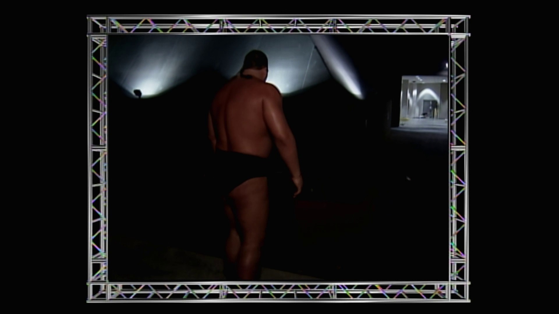 A frame from WWE Raw (June 21, 1999) at 1:13:17. A shirtless wrestler stands in a darkly lit wrestling ring with dramatic spotlight lighting from above. The frame features an ornate silver and purple truss border typical of late 1990s WWE production design, with a small inset monitor visible in the upper right corner.