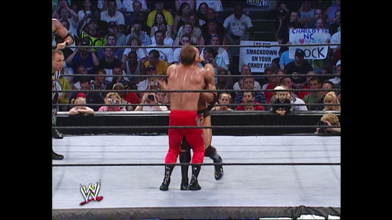 A frame from WWE Raw (August 1, 2002) at 1:12:56. A shirtless WWE wrestler in red and black attire stands in the ring facing an opponent, with a packed crowd visible in the stands behind the ropes. The WWE logo is visible in the lower left corner of the broadcast.