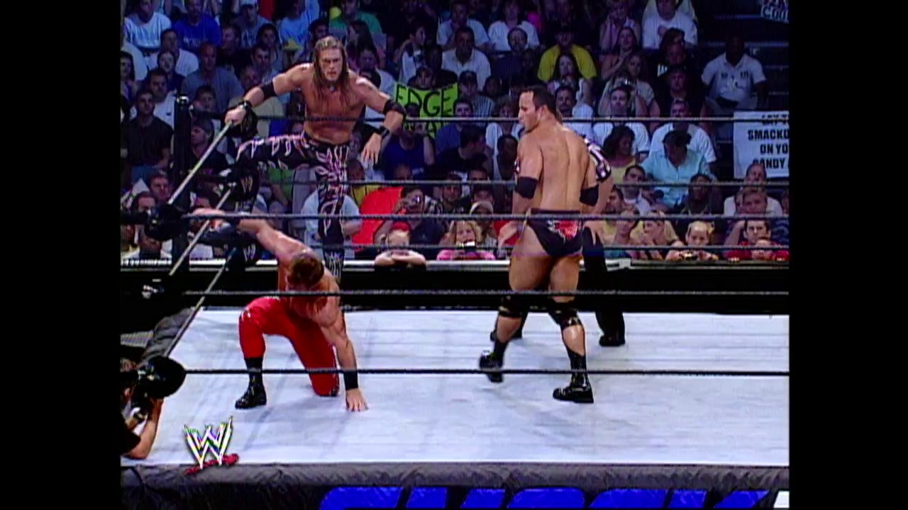 A frame from WWE Raw (August 1, 2002) at 1:13:07. # WWE Raw Match Scene

A WWE wrestling match in progress shows three wrestlers in the ring—one in red clothing on the mat, another shirtless wrestler standing, and a third on the ring apron. The crowd fills the arena in the background while the WWE logo appears in the bottom left corner.