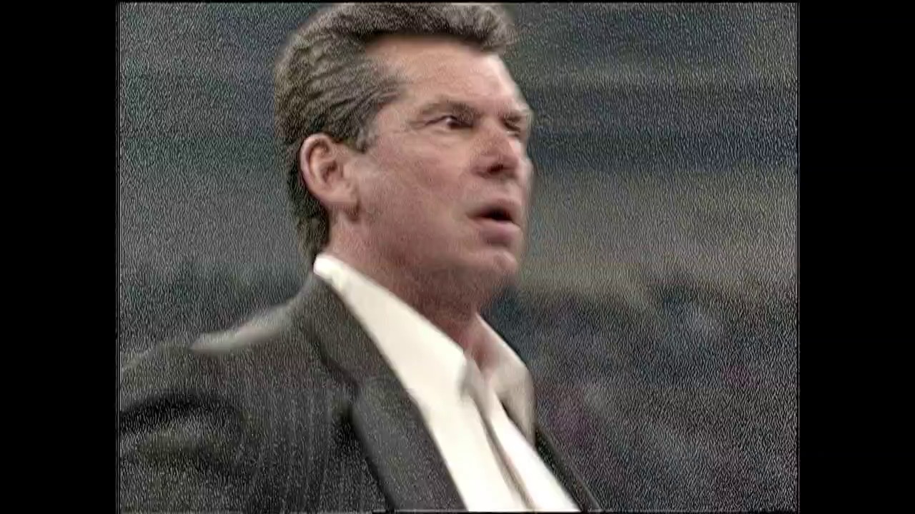 A frame from WWE SmackDown (December 21, 2000) at 1:28. A man in a dark suit and white dress shirt is shown in profile against a gray background, appearing to be speaking or reacting during a WWE broadcast. The image has the characteristic video quality and styling typical of early 2000s professional wrestling television.