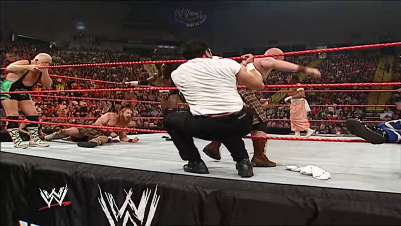 A frame from WWE Raw (April 2, 2007) at 13:40. A WWE wrestler in a white shirt and dark pants executes a move in the red-roped ring while opponents lie on the mat, with a packed crowd visible in the arena background and WWE branding displayed on the ring apron.