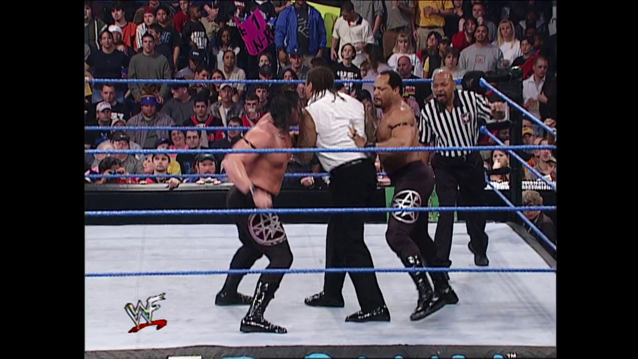 A frame from WWE SmackDown (February 8, 2001) at 53:12. A WWE SmackDown match in progress features two wrestlers in the blue-roped ring with a referee in striped shirt overseeing the action. The packed crowd fills the arena background while the WWF logo is visible on the mat.