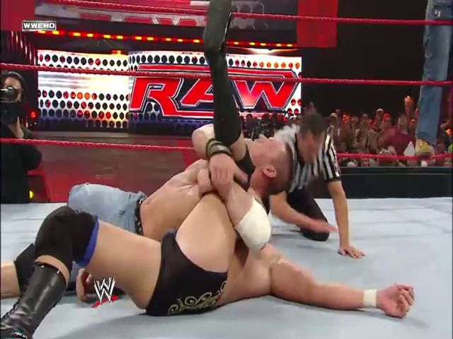 A frame from WWE Raw (July 21, 2008) at 50:44. Two WWE wrestlers engage in a match on the red-roped ring during Raw, with one performer applying a submission hold to their opponent. The arena crowd is visible in the background, along with illuminated WWE graphics and signage typical of the broadcast production.