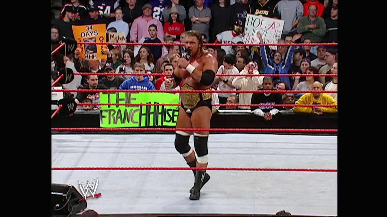 A frame from WWE Raw (February 28, 2005) at 8:28. A shirtless wrestler celebrates in the WWE Raw ring, wearing black wrist and knee tape while holding a championship belt. The crowd is visible behind the red ropes, with a bright green "The Franchise" graphic displayed on the ring apron.