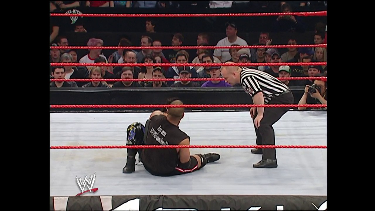 A frame from WWE Backlash (2004) at 22:37. A wrestler lies on the canvas while a referee in black and white stripes stands over him during a WWE match. The red-roped ring is surrounded by an engaged crowd, with the WWE logo visible in the lower left corner.