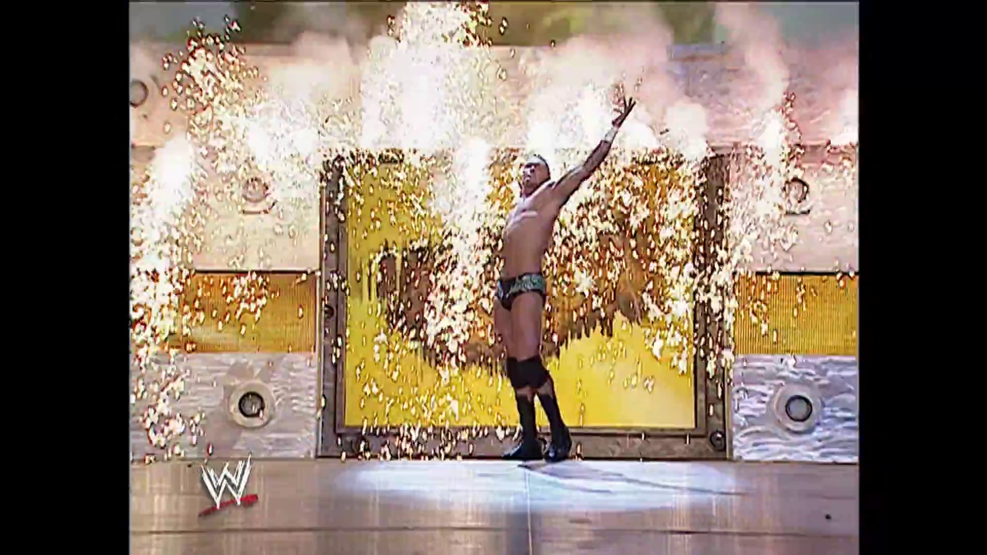 A frame from WWE Raw (September 25, 2006) at 1:02:56. A shirtless WWE wrestler stands triumphantly with his arm raised as gold confetti rains down around him in the ring, with yellow pyrotechnics exploding in the background during a celebratory moment on WWE Raw.
