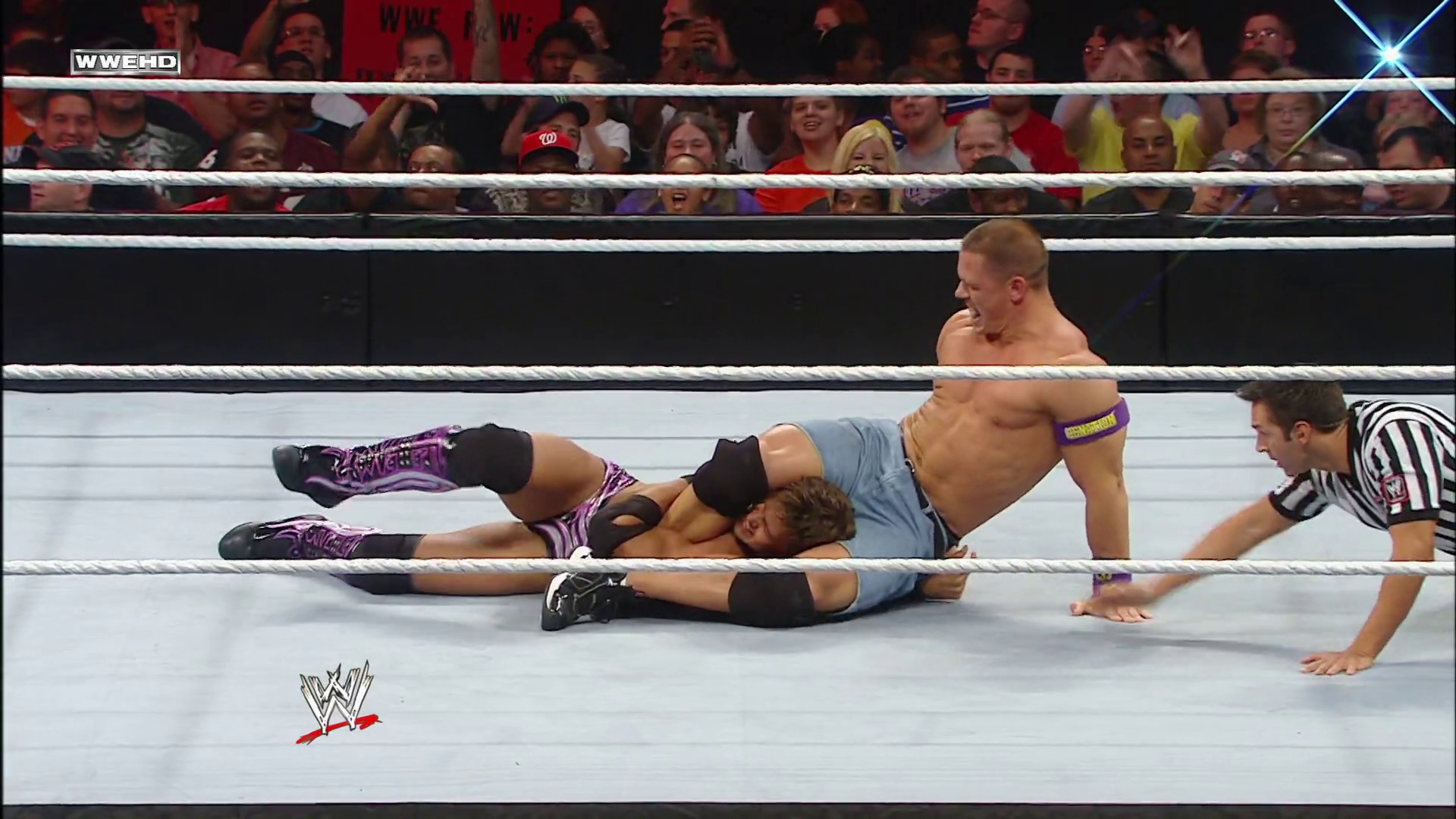 A frame from WWE Raw (September 6, 2010) at 41:40. A WWE wrestler in purple and black attire lies on the canvas after being knocked down, while another shirtless opponent stands nearby. A referee in a striped shirt watches the action as the crowd cheers in the background behind the white ring ropes.