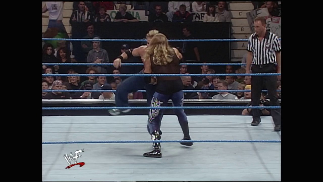 A frame from WWE SmackDown (November 18, 1999) at 6:43. A blonde female wrestler in dark attire stands in a WWE ring with blue ropes, facing off during a match. A referee in a striped shirt stands nearby as the crowd watches from the arena seats, with the WAF logo visible in the lower left corner.
