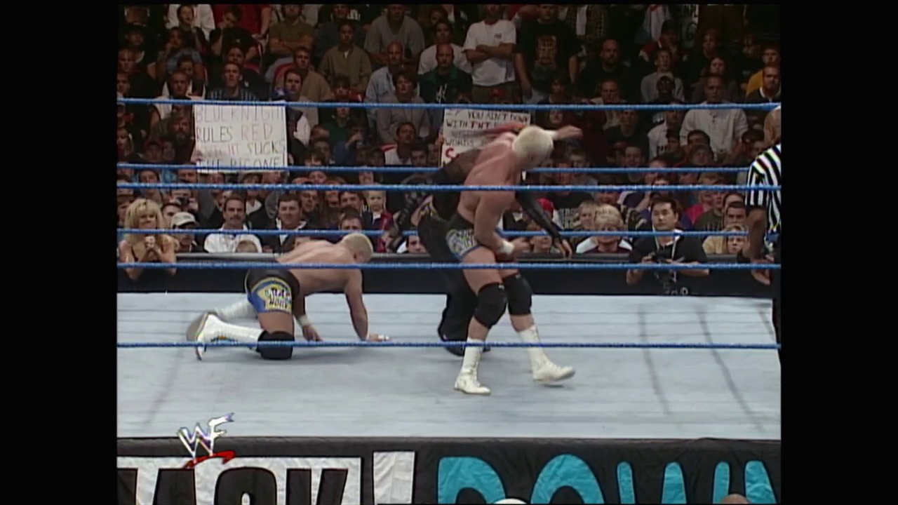 A frame from WWE SmackDown (October 21, 1999) at 1:01:33. Two wrestlers engage in combat inside a WWE ring surrounded by a packed crowd. One wrestler is on the ground while the other stands over him, with a referee visible ringside and the WWF logo displayed at the bottom of the frame.
