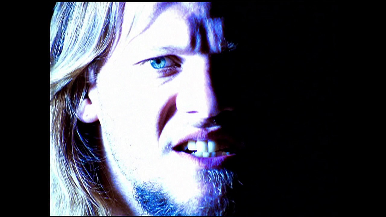 A frame from WWE SmackDown (August 16, 2001) at 0:34. A close-up profile shot of a male wrestler with long blonde hair and facial hair, rendered in blue and purple tones against a black background. The image appears to be a stylized or digitally processed video frame from a wrestling broadcast.