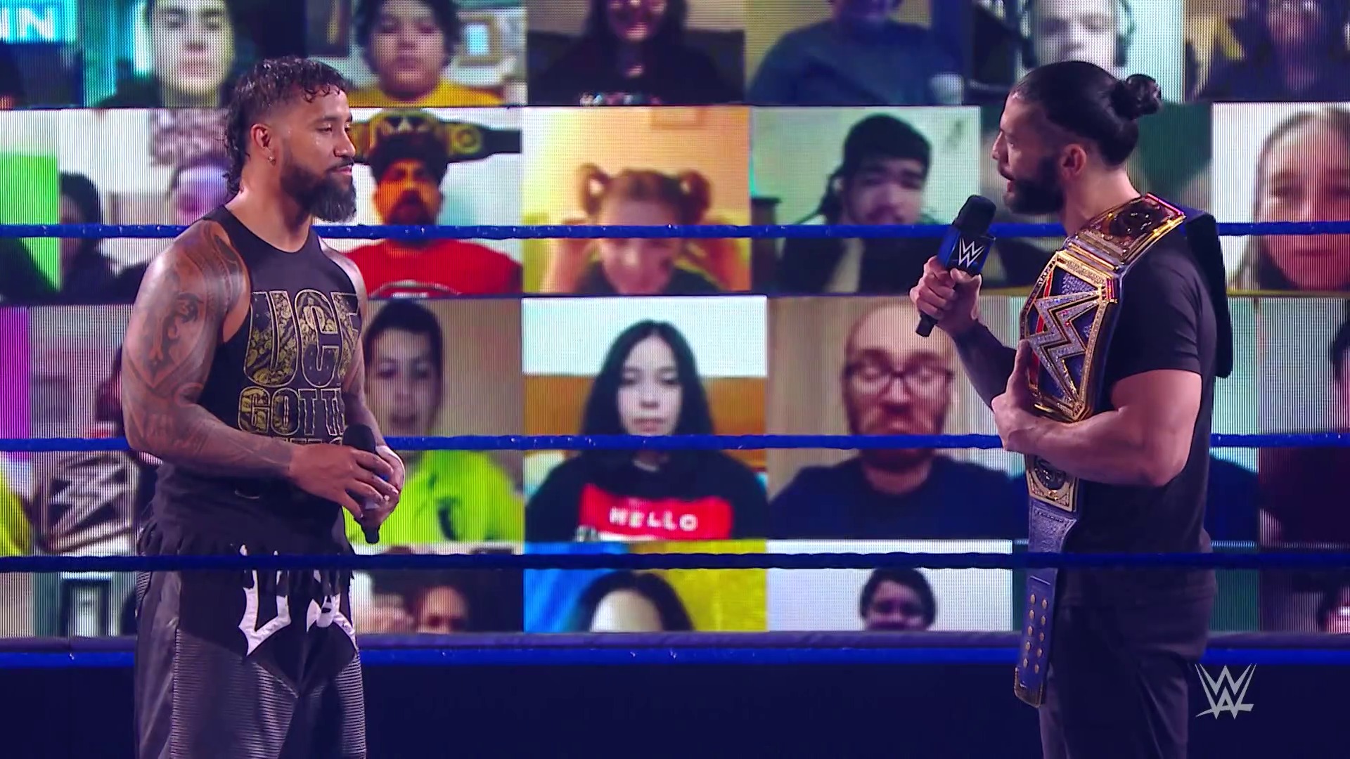 A frame from WWE SmackDown (September 11, 2020) at 11:56. Two WWE wrestlers face off in the ring during a televised SmackDown event, with one holding a championship belt. Virtual crowd screens fill the background due to pandemic-era restrictions, while the blue-roped wrestling ring frames the confrontation.