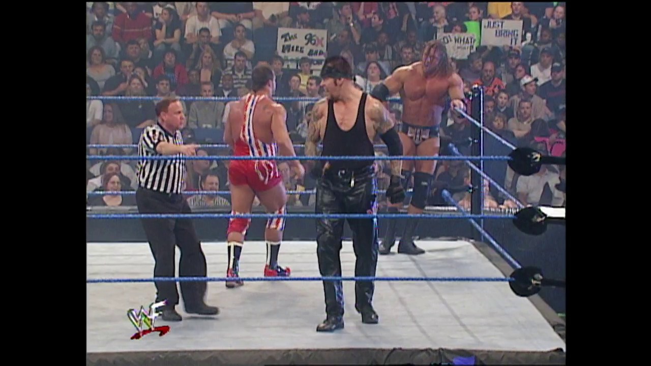 A frame from WWE Raw (January 31, 2002) at 1:01:41. A WWE wrestling match in progress featuring two wrestlers in the ring with a referee overseeing the action. The crowd fills the arena in the background, with visible signage and the distinctive blue WWE Raw ring ropes framing the match.