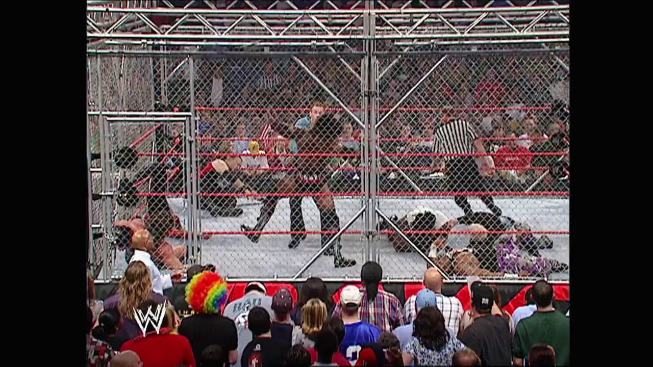 A frame from WWE Raw (October 27, 2003) at 1:34:21. A Hell in a Cell match takes place inside the steel cage structure, with wrestlers grappling on the mat while a referee officiates. The crowd watches intently from ringside, with the WWE logo visible on the barrier.