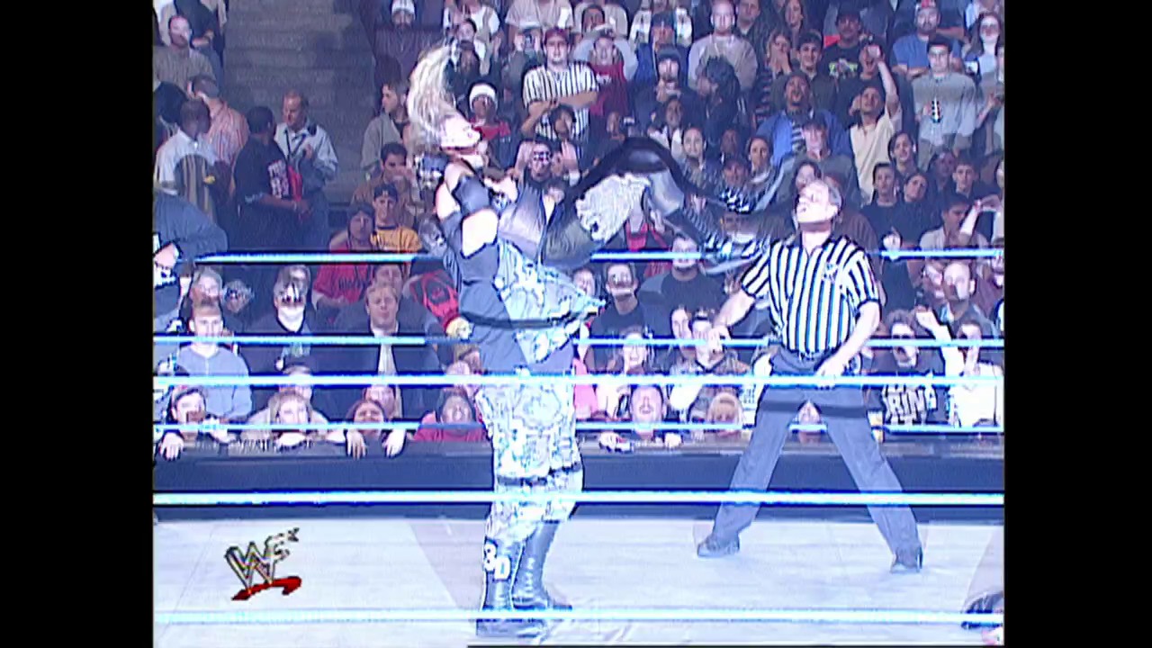 A frame from WWE SmackDown (February 8, 2001) at 39:18. A wrestler in elaborate blue and white attire stands in a WWE ring facing an opponent, with a referee in striped shirt nearby. The crowd fills the arena behind the ropes, and the WWF logo is visible in the lower left corner.