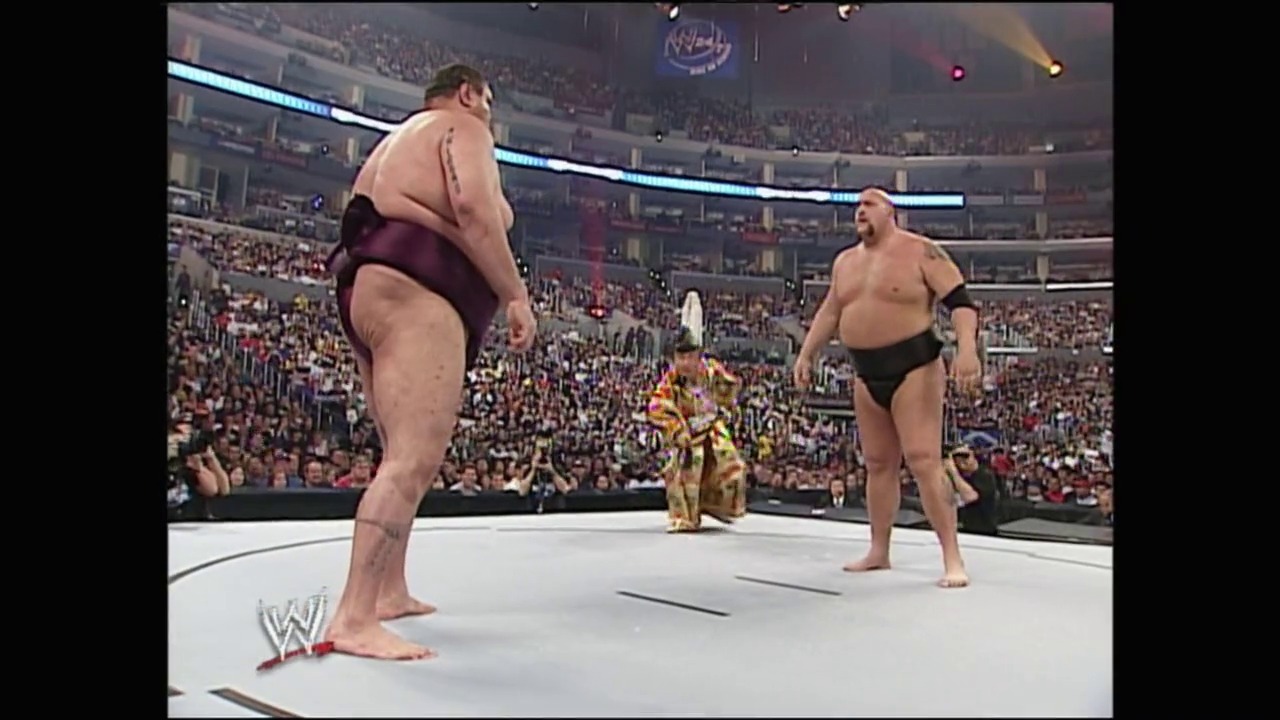 A frame from WrestleMania 21 (2005) at 2:32:25. # WrestleMania 21 Match Frame

Two wrestlers face off in a WWE ring before a packed stadium crowd. The wrestler on the left wears maroon/purple trunks while the one on the right wears black trunks, with a referee in a gold shirt positioned between them.