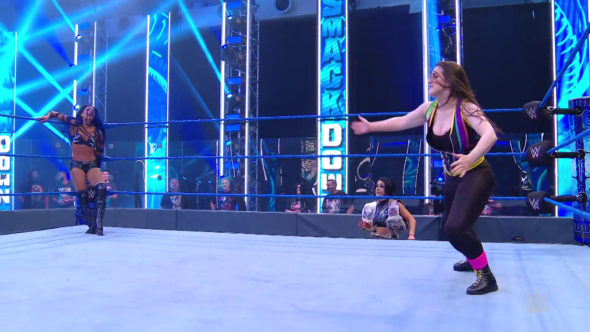 A frame from WWE SmackDown (June 19, 2020) at 1:12:59. # WWE SmackDown Match Scene

A female wrestler in black and pink attire strikes a wrestling pose in the ring, with an opponent visible on the mat. The arena features bright blue neon lighting and graphics, with spectators visible in the background behind the wrestling ring.