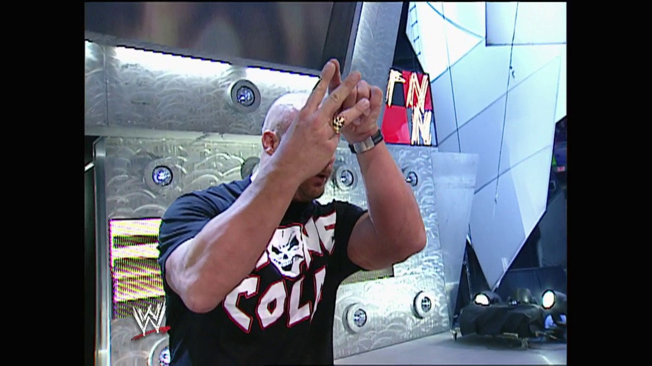 A frame from WWE Raw (March 10, 2003) at 1:29:07. A wrestler in a black and red "SOLI" shirt stands in the ring with his hands raised near his head in a celebratory pose. The WWE logo is visible on the left side, with decorative panels and lighting fixtures visible in the background of the arena.
