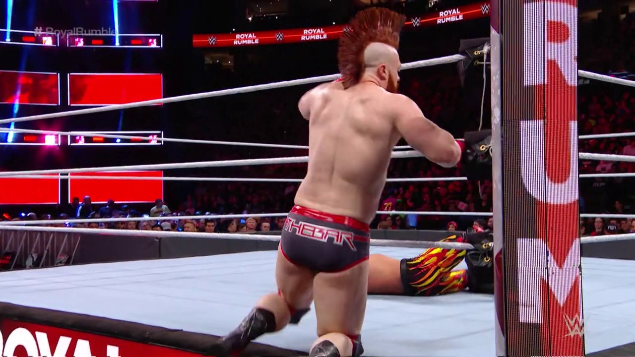 A frame from WWE Royal Rumble (2018) at 2:22:06. A shirtless wrestler with red hair and beard stands in a WWE ring during Royal Rumble 2018, while another competitor lies on the mat. The arena is lit with red and blue neon signage, with spectators visible in the darkened crowd.