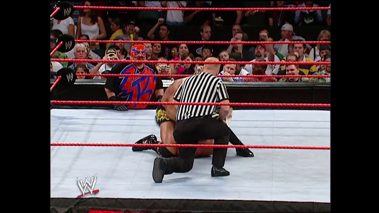 A frame from WWE Raw (January 10, 2005) at 27:48. A referee in a black and white striped shirt counts over a wrestler lying on the mat in the WWE ring, while the crowd watches from the stands behind the red ropes. The wrestler wears red and blue attire with a distinctive mask.