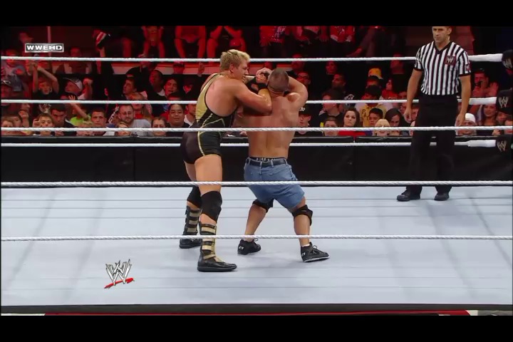 A frame from WWE Raw (August 8, 2011) at 13:47. Two wrestlers grapple in the WWE ring during an intense match, with one performing a headlock on his opponent. A referee in a striped shirt stands nearby as the crowd watches from the arena seats, with the WWE logo visible on the ring mat.