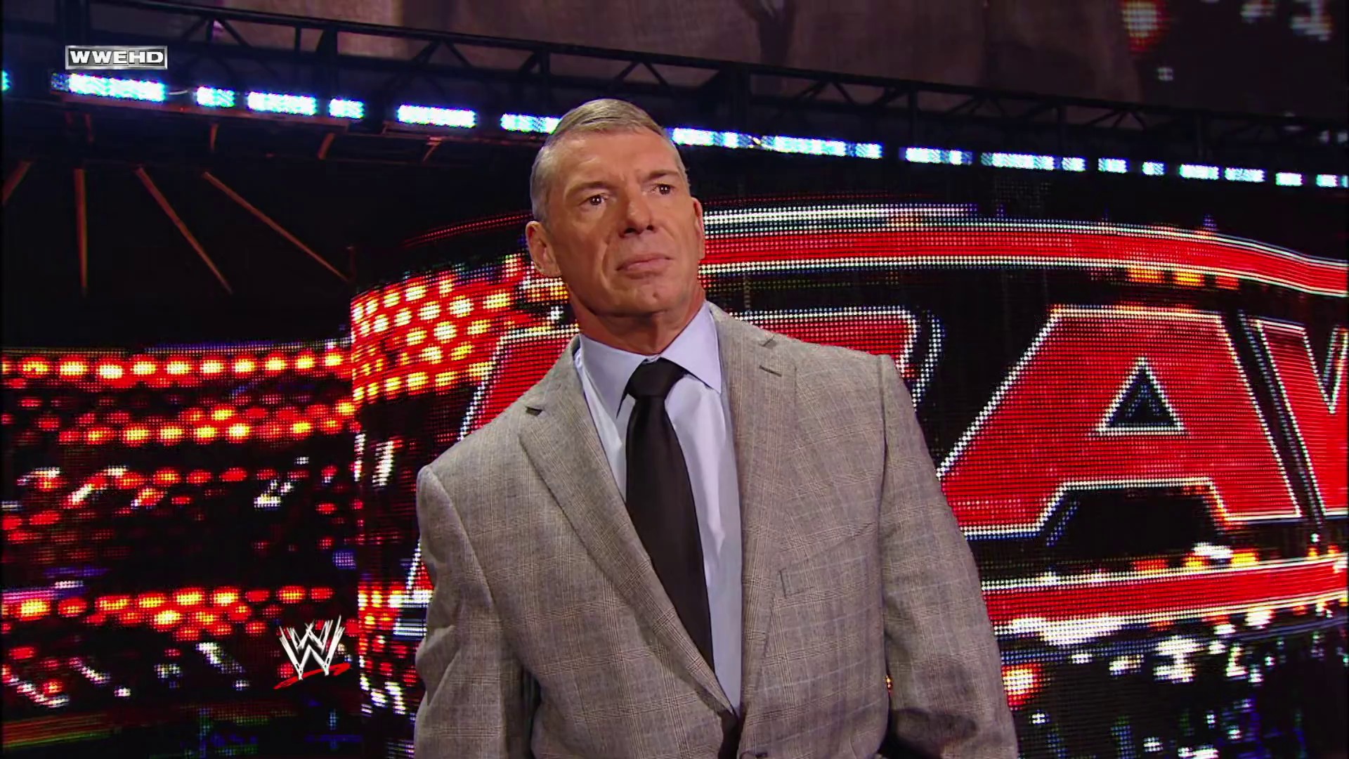 A frame from WWE Raw (February 22, 2010) at 14:21. A man in a gray blazer and dark tie stands in a WWE Raw arena, with the illuminated red "Raw" logo and LED screens visible behind him. The WWE and WWEHD logos are displayed in the upper corners of the frame.