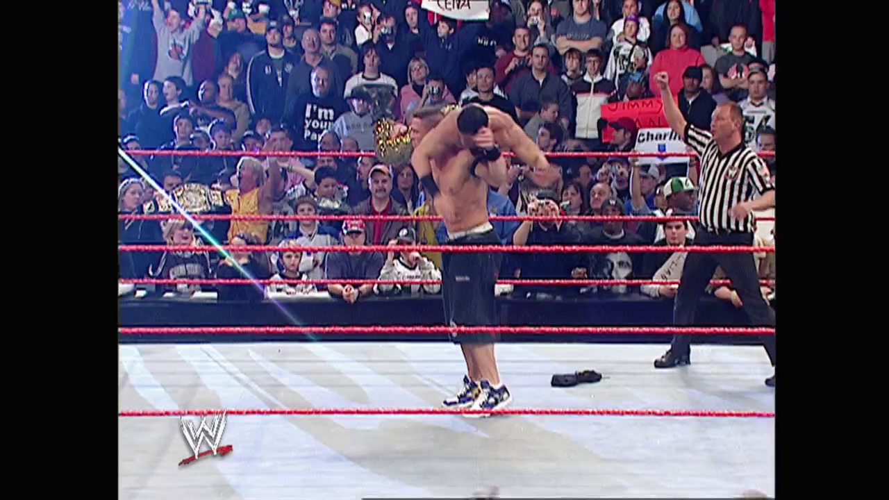 A frame from WWE Raw (December 12, 2005) at 1:30:22. A shirtless wrestler performs in a WWE Raw match inside a red-roped ring, with a referee in striped shirt observing nearby. The crowd fills the arena stands behind the ropes, while the WWE logo appears in the bottom left corner.