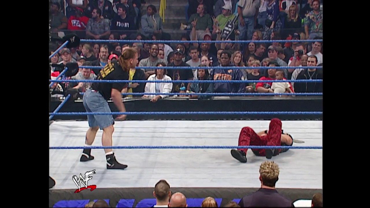 A frame from WWE SmackDown (December 20, 2001) at 49:23. A WWE wrestler in a denim outfit stands in the ring near an opponent lying on the mat in red attire. The crowd fills the background behind the blue-roped ring, with the WWF logo visible in the corner.