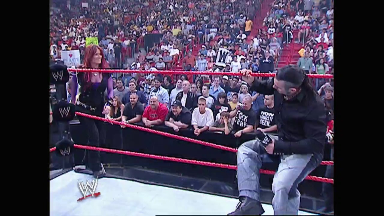 A frame from WWE Raw (June 21, 2004) at 1:09:17. A WWE wrestler sits on the ring apron in a black shirt and jeans, addressing the enthusiastic crowd in a packed arena. The red ropes and ringside fans are visible, with the WWE logo displayed prominently on the mat and barriers.
