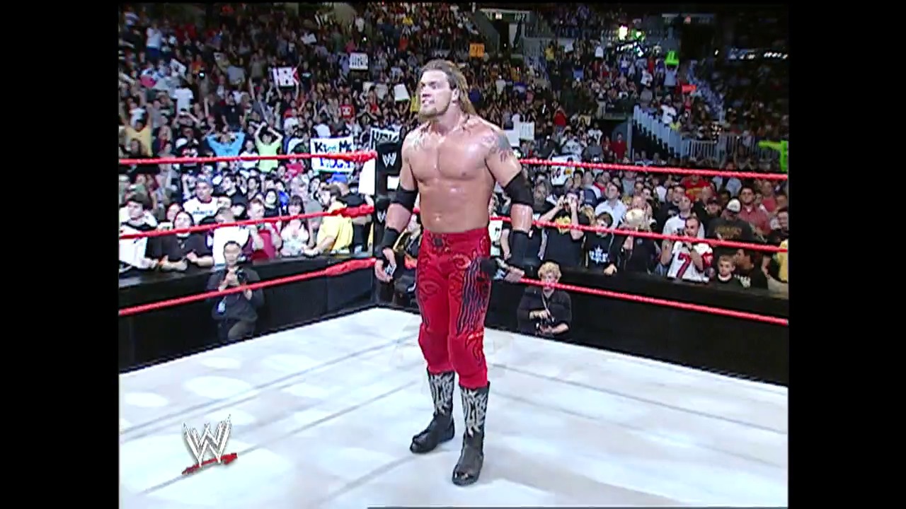 A frame from WWE Raw (January 10, 2005) at 41:14. A muscular wrestler in red patterned pants and black wrist tape stands in a WWE ring surrounded by a packed crowd. The white mat is bordered by red ropes, with the WWE logo visible in the corner and spectators filling the arena stands.