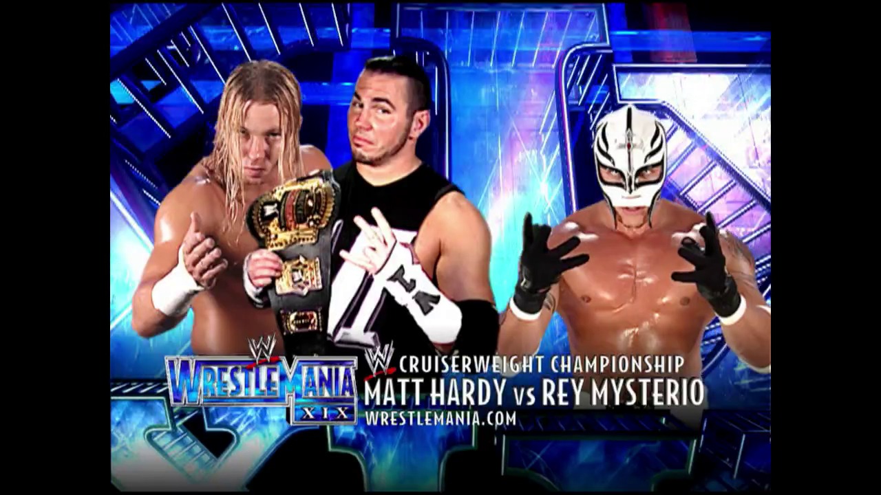 A frame from WWE SmackDown (March 27, 2003) at 1:00:03. # WWE WrestleMania XIX Cruiserweight Championship Match Promo

A wrestling promotional graphic displays Matt Hardy (left, holding championship belt) and Rey Mysterio (right, in white mask) facing off for the Cruiserwaight Championship at WrestleMania XIX, set against a blue-lit arena backdrop with WWE branding.