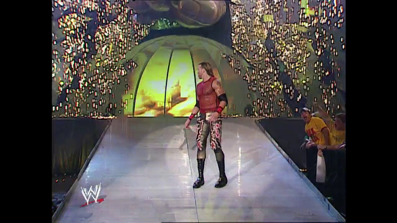 A frame from WWE Raw (May 23, 2002) at 38:39. A WWE wrestler in a red and patterned outfit stands on an illuminated walkway surrounded by pyrotechnic effects and golden sparkles. The entrance features a large glowing tunnel structure with dramatic lighting effects as the crowd watches from the sides.