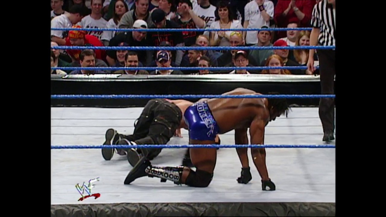 A frame from WWE Raw (February 28, 2002) at 59:36. A wrestler in blue shorts performs a move over an opponent lying on the white WWE ring canvas, while a crowd watches from the stands behind the blue ropes. The WWF logo is visible in the lower left corner of the broadcast.