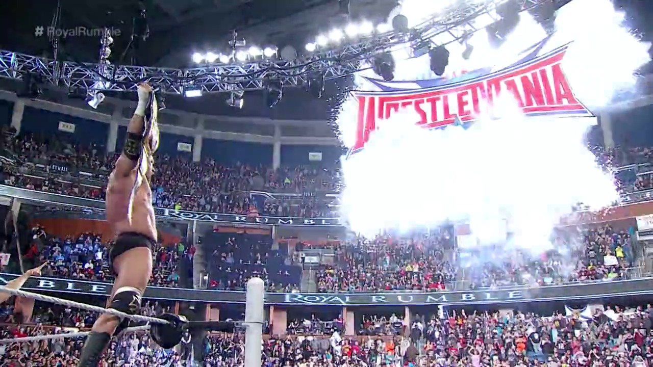 A frame from WWE Royal Rumble (2016) at 2:59:09. A wrestler stands victorious with arm raised in the WWE ring at Royal Rumble 2016, with the event logo displayed on the massive screen above and a packed crowd visible throughout the arena's multiple levels.
